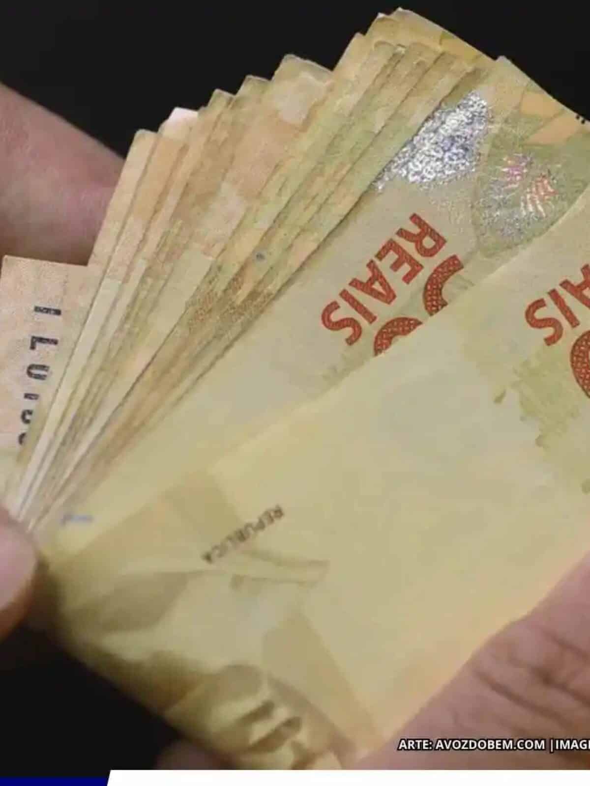 Pessoa segurando cédulas de real, representando a previsão de aumento do salário mínimo para R$ 1.741 em 2027.