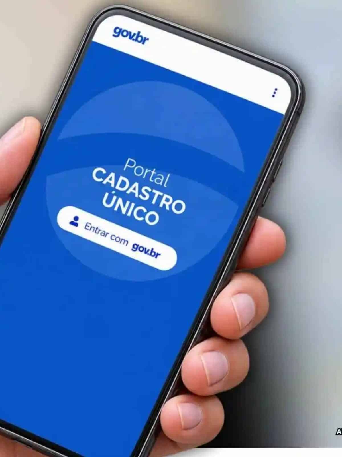 Pessoa segurando celular com acesso ao Cadastro Único, representando a indisponibilidade temporária do sistema para manutenção e processamento da base de dados.
